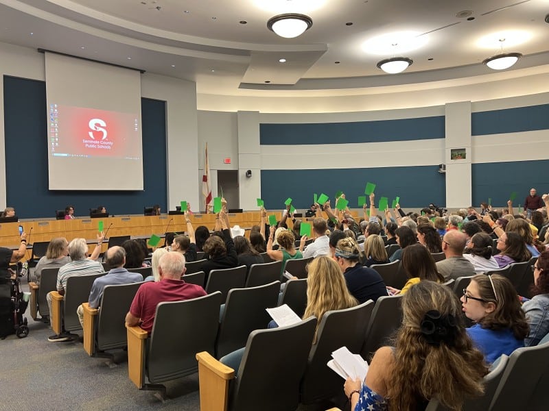An image shows audience members at Tuesday night's Seminole County School Board meeting holding up placards to show whether they agreed or disagreed with the speaker. One side was red (showing disagreement) and the other side was green (showing agreement).